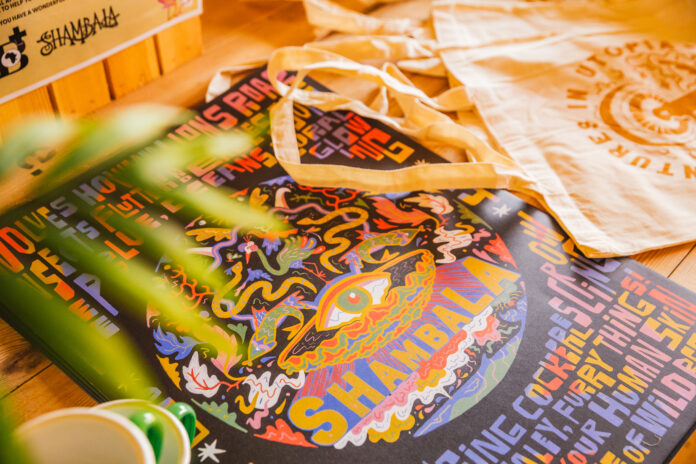 A photograph of some official Shambala merchandise - including a tote bag and an art print.